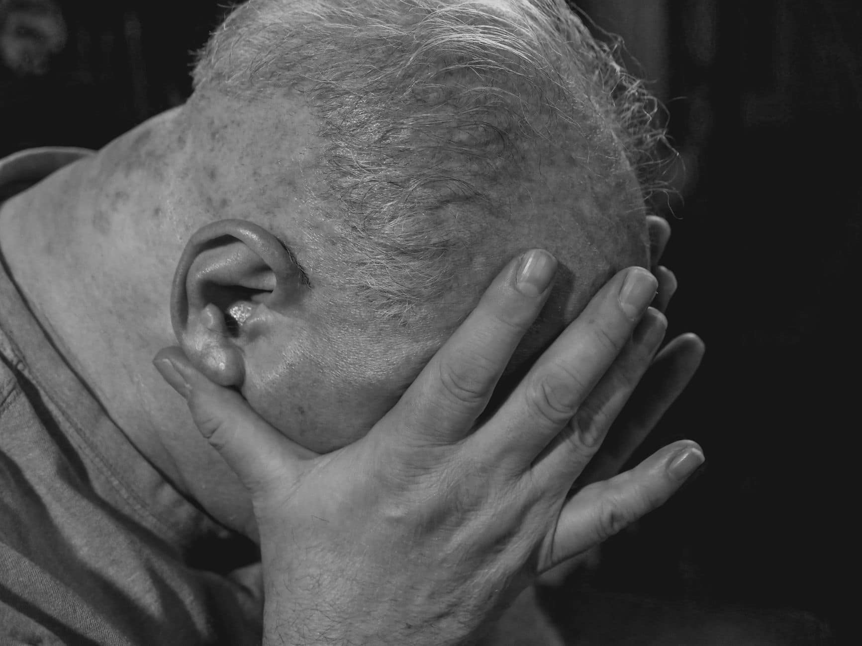 a close up shot of an elderly man covering his face